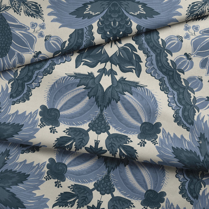 Flowering Pomegranate in linen and dusty blue: an ogee lattice of lace borders framing a blossom held between two swelling pomegranates, translated from an 18th-century French block-printed quilt. draped fabric fold preview.